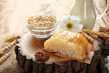 Composition of honeycomb, oatmeal and milk on wooden background