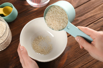 Cooking concept. Woman pouring rice from measuring scoop to bowl on kitchen table