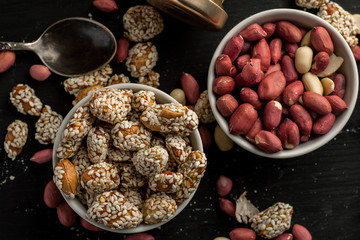 Two ceramic bowls with peanuts on a black wooden table, top view
