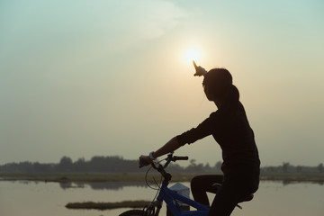 Silhouette biker-girl at the sunset on the meadow
