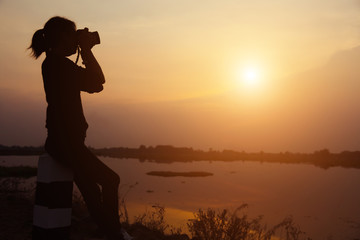 Fototapeta premium Silhouette women Nature photographer with digital camera on the mountain and lake