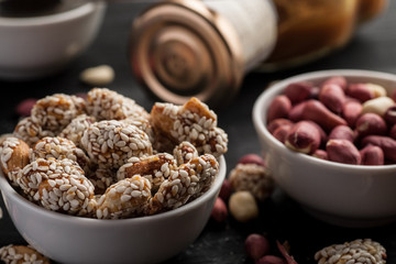 Peanuts in ceramic bowls and bottle with caramel on a wooden table, selective focus