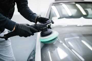Car detailing - Hands with orbital polisher in auto repair shop. Selective focus. 
