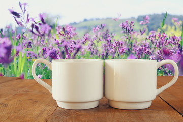 Fototapeta premium Two cups of coffee a wooden table in front of spring landscape