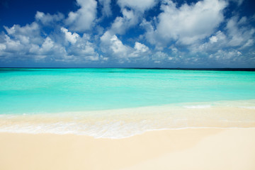 Tropical beach. Ocean waves and cloudy sky background. White sand and crystal-blue sea. Ocean water nature, beach relax. Summer sea vacation. Maldives islands sea background