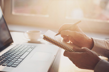 Young man is working, using laptop computer and writing in his notebook
