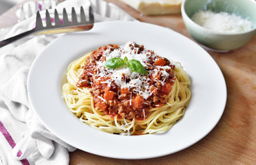 Spaghetti Bolognese on a white plate with decorative basil leaf. Italian cuisine, pasta with tomato sauce and parmesan cheese.