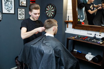 Great time at barbershop. Cheerful young bearded man getting haircut by hairdresser while sitting in chair at barbershop