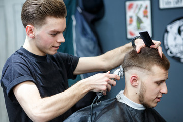 Great time at barbershop. Cheerful young bearded man getting haircut by hairdresser while sitting in chair at barbershop