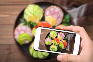 Hands taking photo bagel sandwiches with soft cheese  and vegetables with smartphone.
