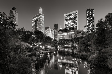 Midtown Manhattan skyscrapers illuminated in evening.The buildings of Central Park South are reflected in the Pond. New York City. Black & White