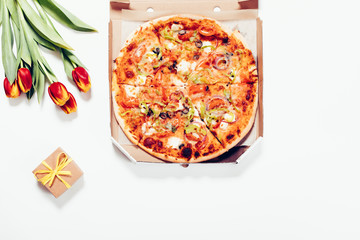 Pizza box, red tulips and a small gift box lying on white table