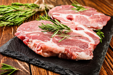 Raw pork steaks with seasonings on a wooden surface