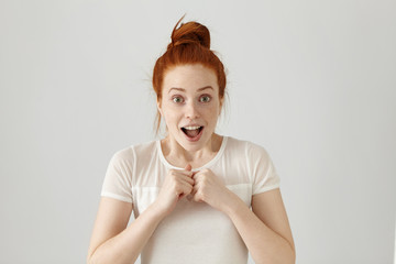 Portrait of happy excited young woman with ginger hair screaming or exclaiming, opening mouth...