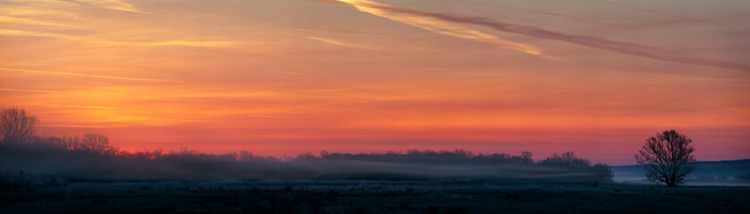 Obraz premium Panoramic view of the rising sun over a misty meadow. Early morning in the spring.