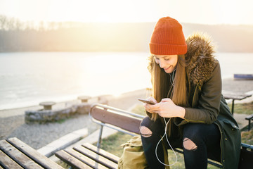 Cheerful hipster girl with smart phone sitting on the bench outdoors