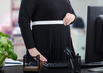 Businesswoman in black dress measures her waist in front of monitor