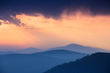 Fantastic sunrise above peaks of smoky mountain with the view into misty hills. Dramatic overcast sky. Mountains silhouettes.