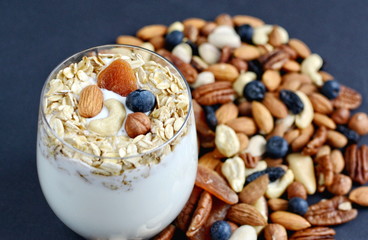 Vitamin breakfast yogurt cocktail with blueberries, oat flakes, dried fruits and nuts in glass. Black background
