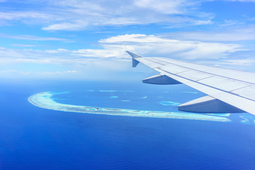 Looking thru airplane 's window seeing wing of airplane , white clouds , blue sky and Maldives islands