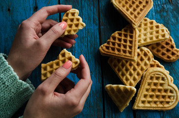 Female hands holding home made heart shaped waffles on rustic table