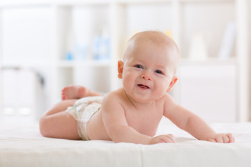 Baby infant boy wearing diaper lying in bed in white light bedroom or nursery. Textile and bedding for children.