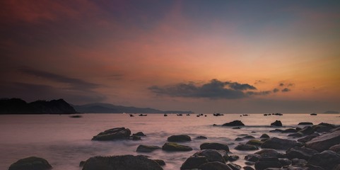 Fototapeta premium A fiery orange morning sky looking out over the south China sea in Vung Lam Bay Vietnam. With a rock covered coastline and fishing boat silhouettes coming and going.