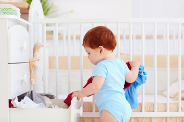 funny infant baby throwing out clothes from the dresser at home