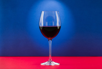 Polished still life glass of wine with nice light effect in red and blue background