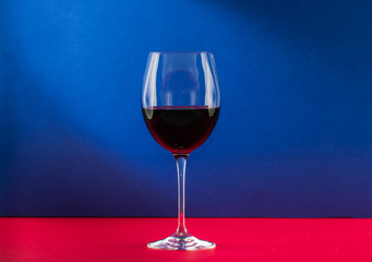 Polished still life glass of wine with nice light effect in red and blue background