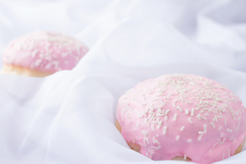 Fototapeta na wymiar Two pink glazed donuts with sprinkles on a white silky background