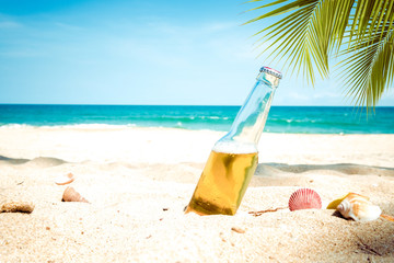Fototapeta na wymiar Beer bottle on a sandy beach with palm tree. vintage color tone effect