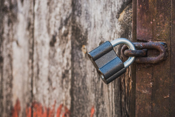 Closeup of old wooden weathered door with peeling paint and new grey metal padlock. Contrast concept. Horizontal color photography.