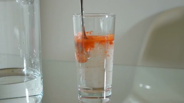 A spoonful of paprika powder is added to the tall glass with pure water and mixed