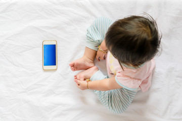 Baby playing or watching movie on smart phone white on bed