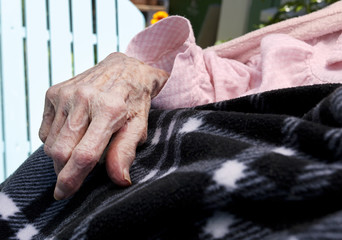 Obraz premium Elderly senior woman's hand resting on blanket.