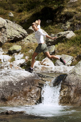 femme souriant qui saute au dessus d'une rivière sur des rochers