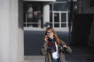 Fototapeta premium a bohemian style woman with red hair is talking on the phone, in a modern architecture environment, while holding a cup of coffee