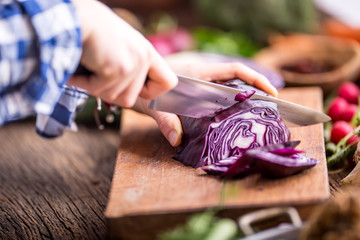 Obraz premium Hand cutting vegetables.Women hands is slicing cabbage on wooden board near vegetables.
