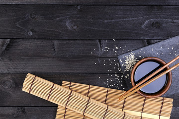 Background for sushi. Bamboo mat, soy sauce, chopsticks on dark table. Top view with copy space