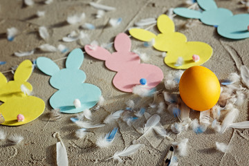 Yellow egg and Garland with colorful paper rabbits and feathers on concrete background. Concept Easter. Top view.