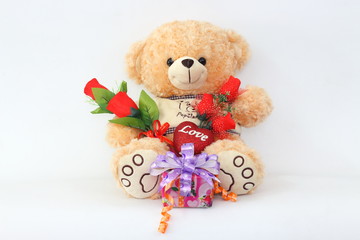 Brown teddy bear with a red rose and a gift box on a white background.