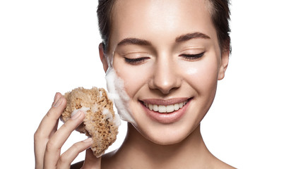 Beautiful girl cleans the skin natural sponge and cleaning foam for the face. On a white background.