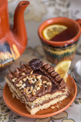 Delicious and sweet chocolate cake with cream and nuts and a сup of black tea with lemon. tea set with teapot, saucer and сup