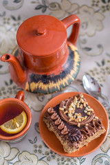 Delicious and sweet chocolate cake with cream and nuts and a сup of black tea with lemon. tea set with teapot, saucer and сup