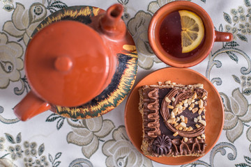 Delicious and sweet chocolate cake with cream and nuts and a сup of black tea with lemon. tea set with teapot, saucer and сup