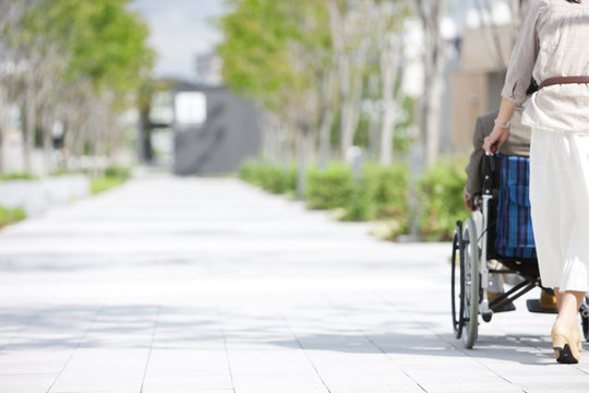 Mature woman pushing senior man on wheelchair, rear view