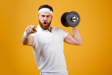 Screaming sportsman holding dumbbell and pointing at camera