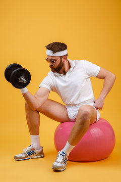 Vertical image of sportsman sitting on fitness ball with dumbbell