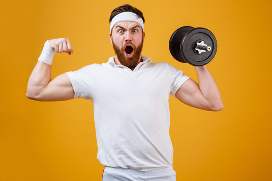 Screaming sportsman holding dumbbell and showing bicep
